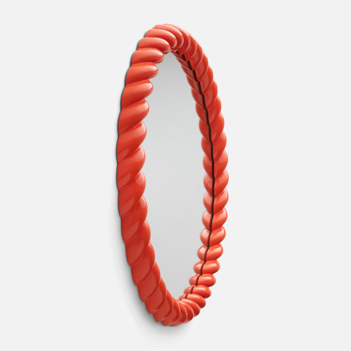 Angled view of Fernand Mirror showcasing its twisted Persimmon-Gloss frame on a white background