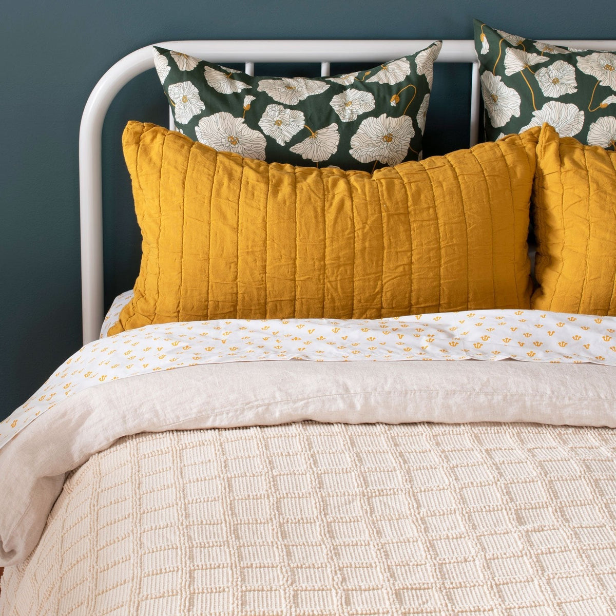 Close-up view of Blooming Field Sham showcasing green poppy print with a dark wall and layered bedding