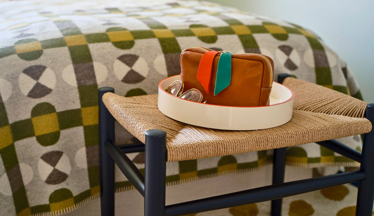 Woven bench displays a cream tray and brown pouch against a geometric patterned blanket