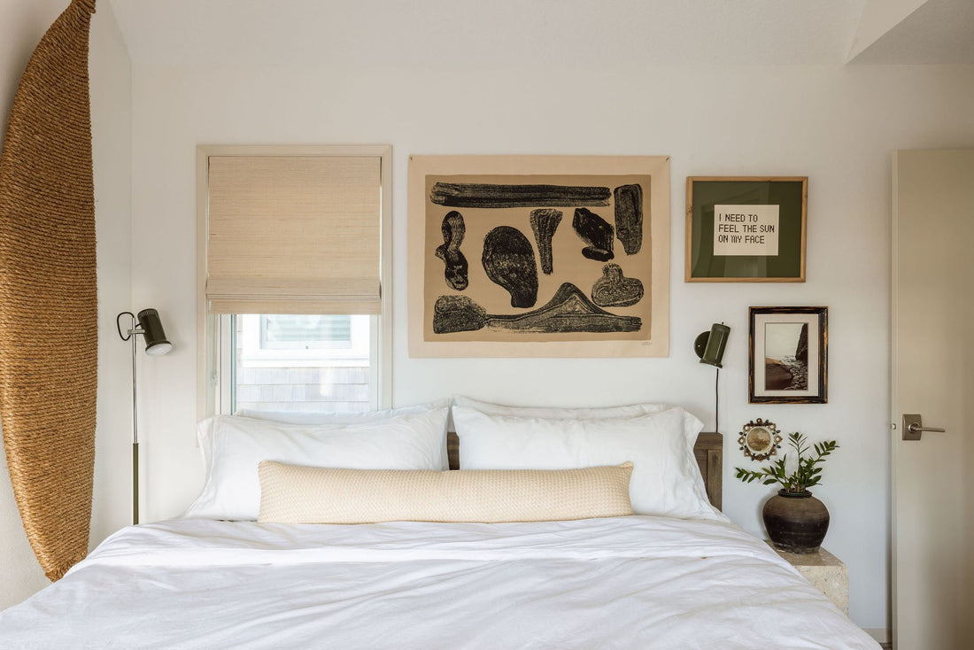 Two floor lamps flank a neatly made bed in a small, art-filled bedroom