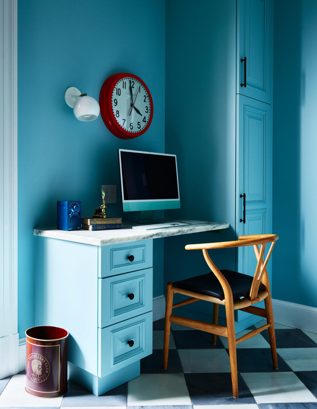 Blue home office features a marble-top desk, computer, wall clock, chair, and matching blue cabinets