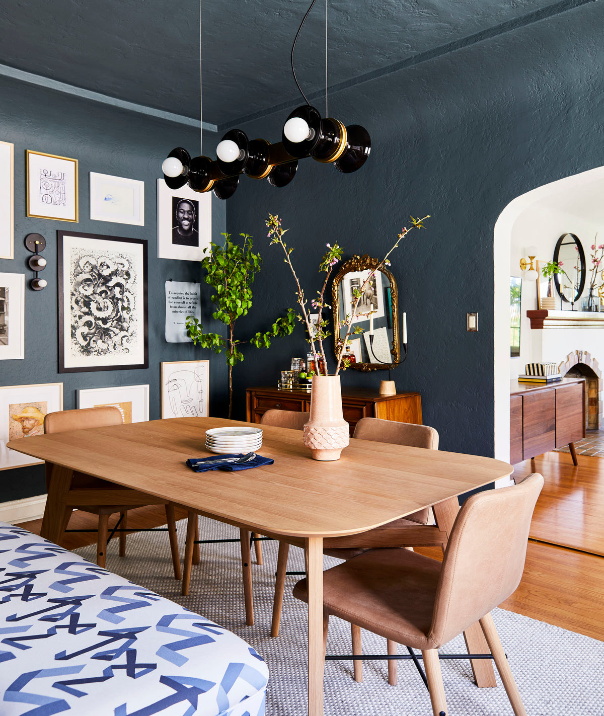 Regent chandelier suspended over a wood dining table in a moody dining room with dark teal textured walls and a gallery wall
