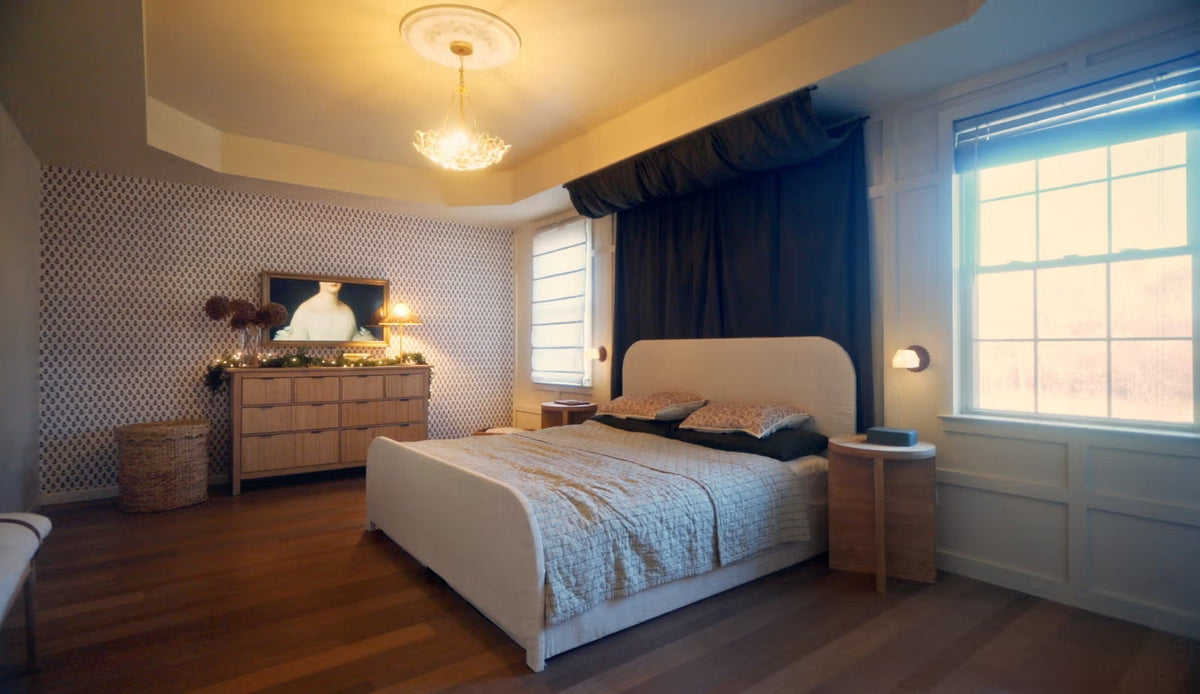 Parisian-inspired bedroom with a curved upholstered bed, patterned walls, dark drapes, and large windows