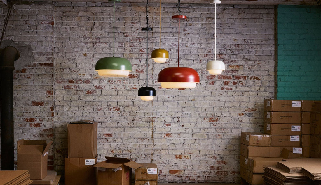 Six colorful pendant lamps from the Benchmade Ray Collection hang against a brick wall in a workshop