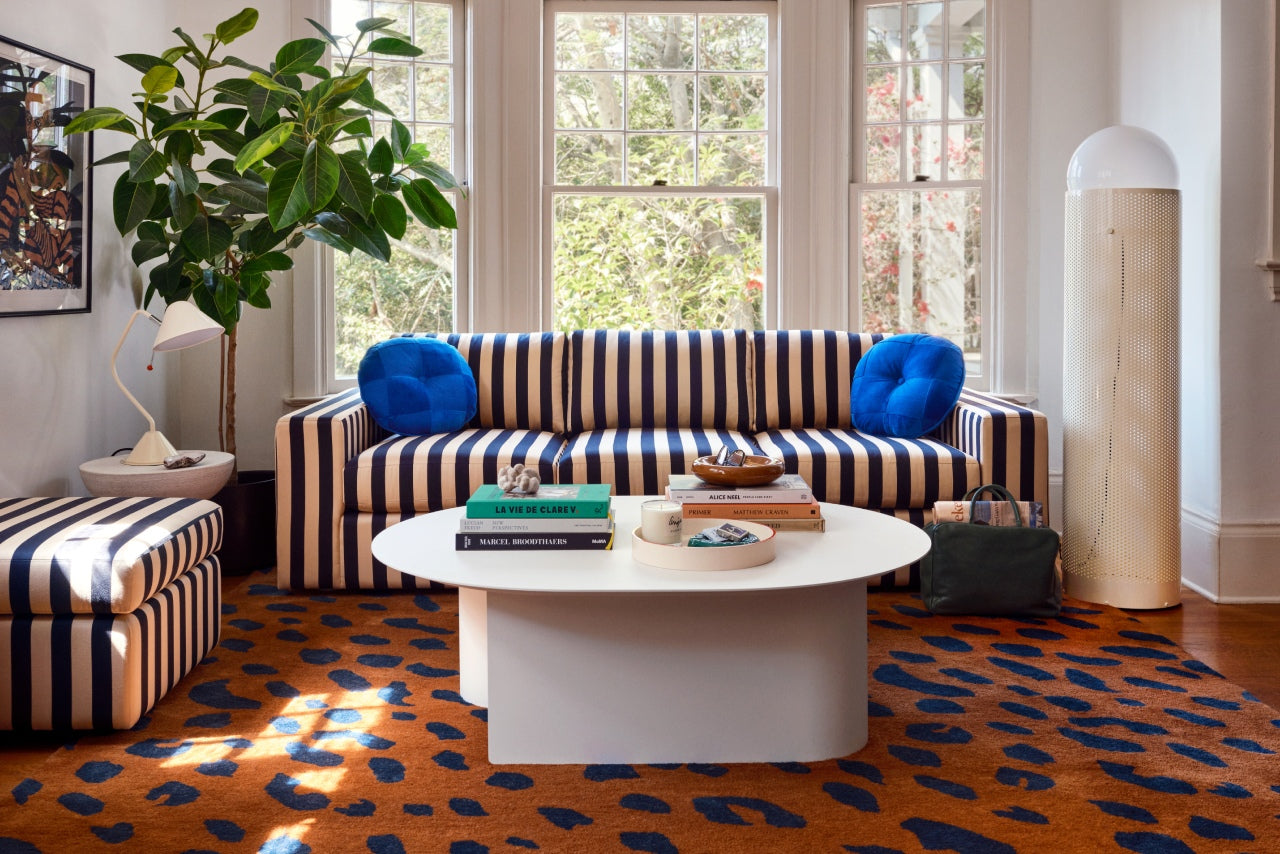 Blue-and-cream striped sofa and ottoman in a bright living room with a white coffee table, plant, and patterned rug
