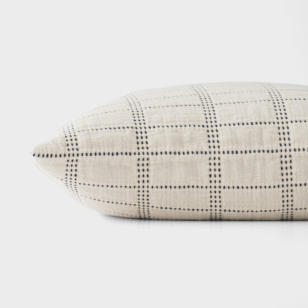 Close-up side view of the Grid Stitch Pillow Cover showcasing a dark blue stitched grid on ivory fabric against a light gray background