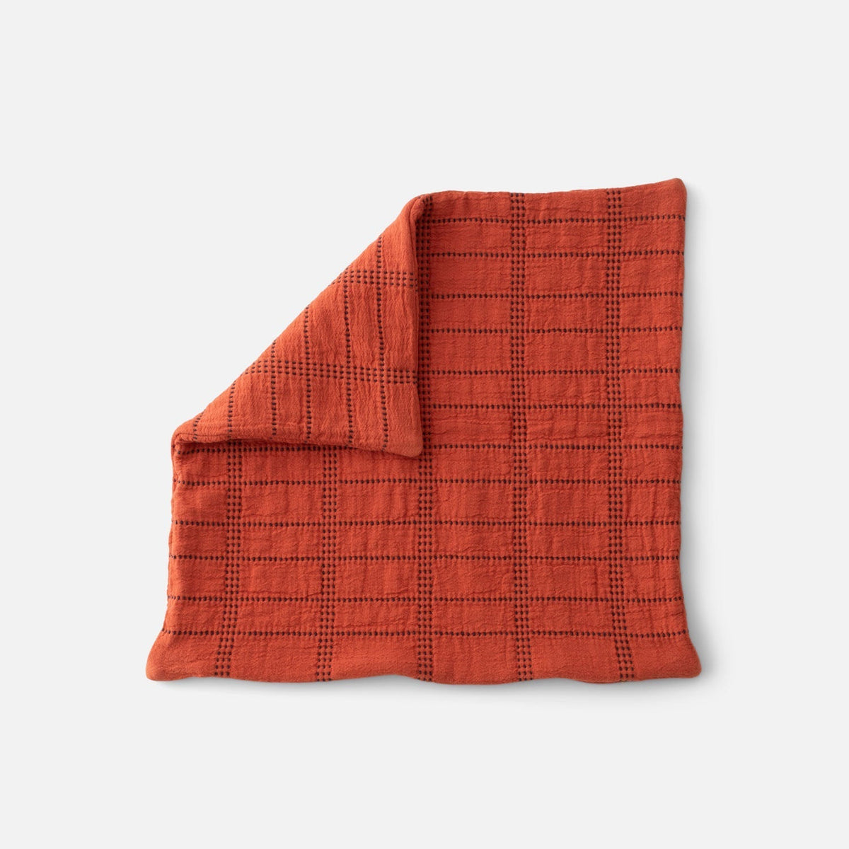 Front view of Grid Stitch Pillow Cover showcasing a rust-colored grid pattern and folded corner on a light gray background
