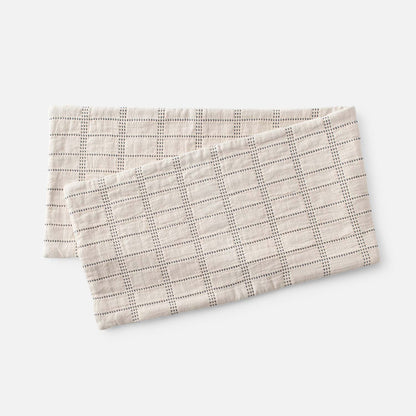 Angled view of Grid Stitch Pillow Cover showcasing its dark stitched grid pattern with overlapping covers on a light background
