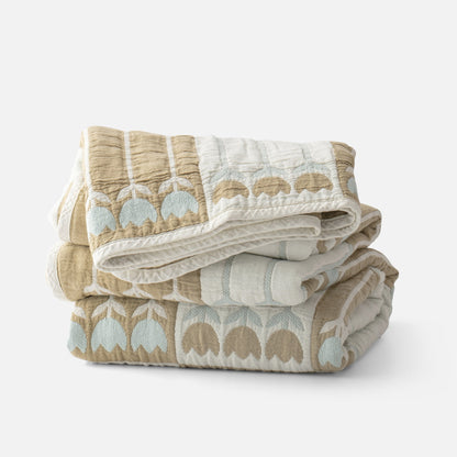 Folded view of the Tulbend Quilt showcasing tan and light blue arch pattern with a white background