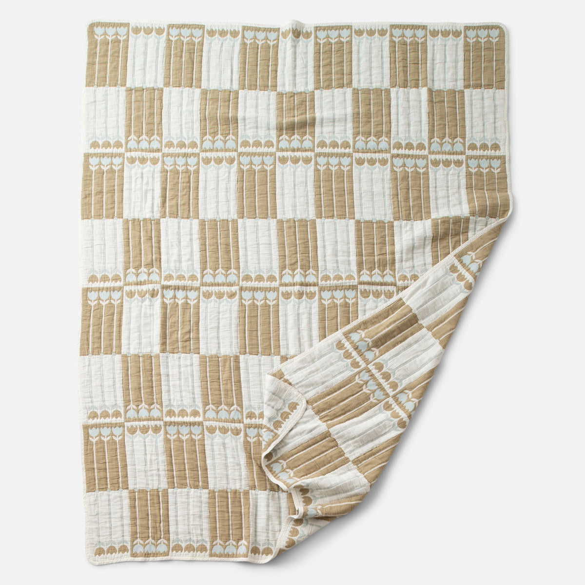 Front view of Tulbend Quilt showcasing a tan and white repeating tulip pattern with a folded corner on a light gray background