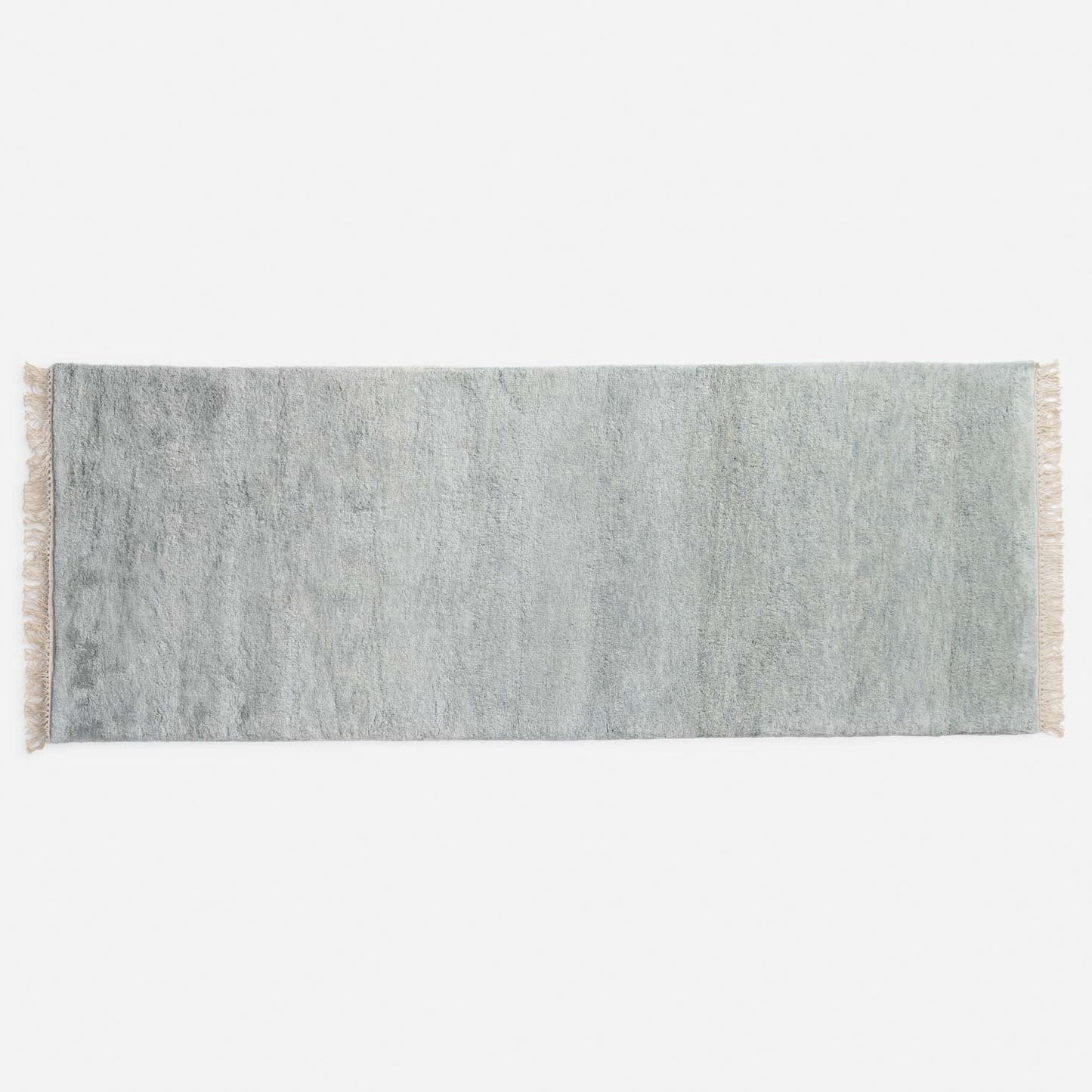 Top-down view of green Mesa Wool Rug showcasing hand-loomed cut pile and tasseled fringe on a white studio background