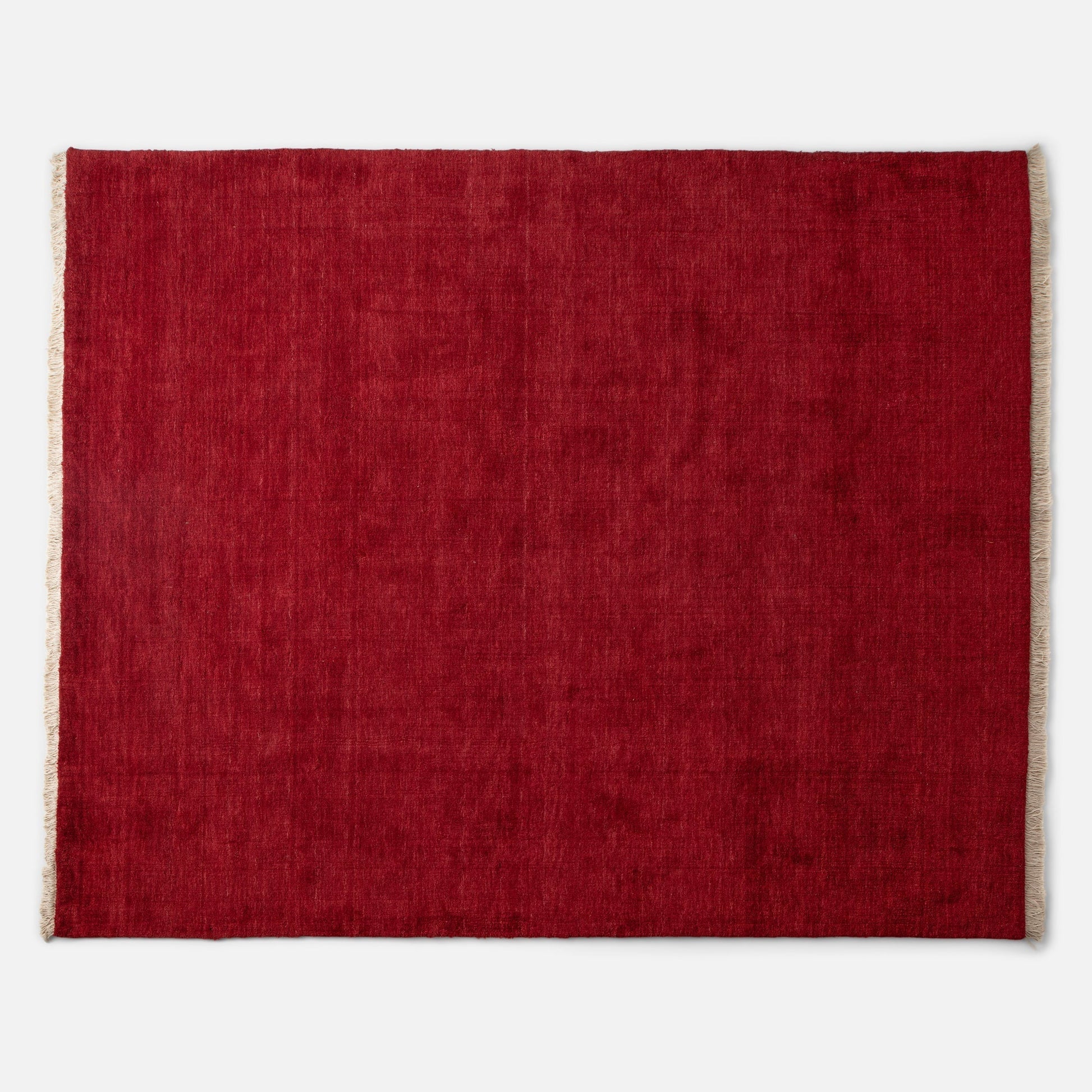 Top edge view of Mesa Wool Rug showcasing red hand-loomed wool pile and natural fringe on a white background
