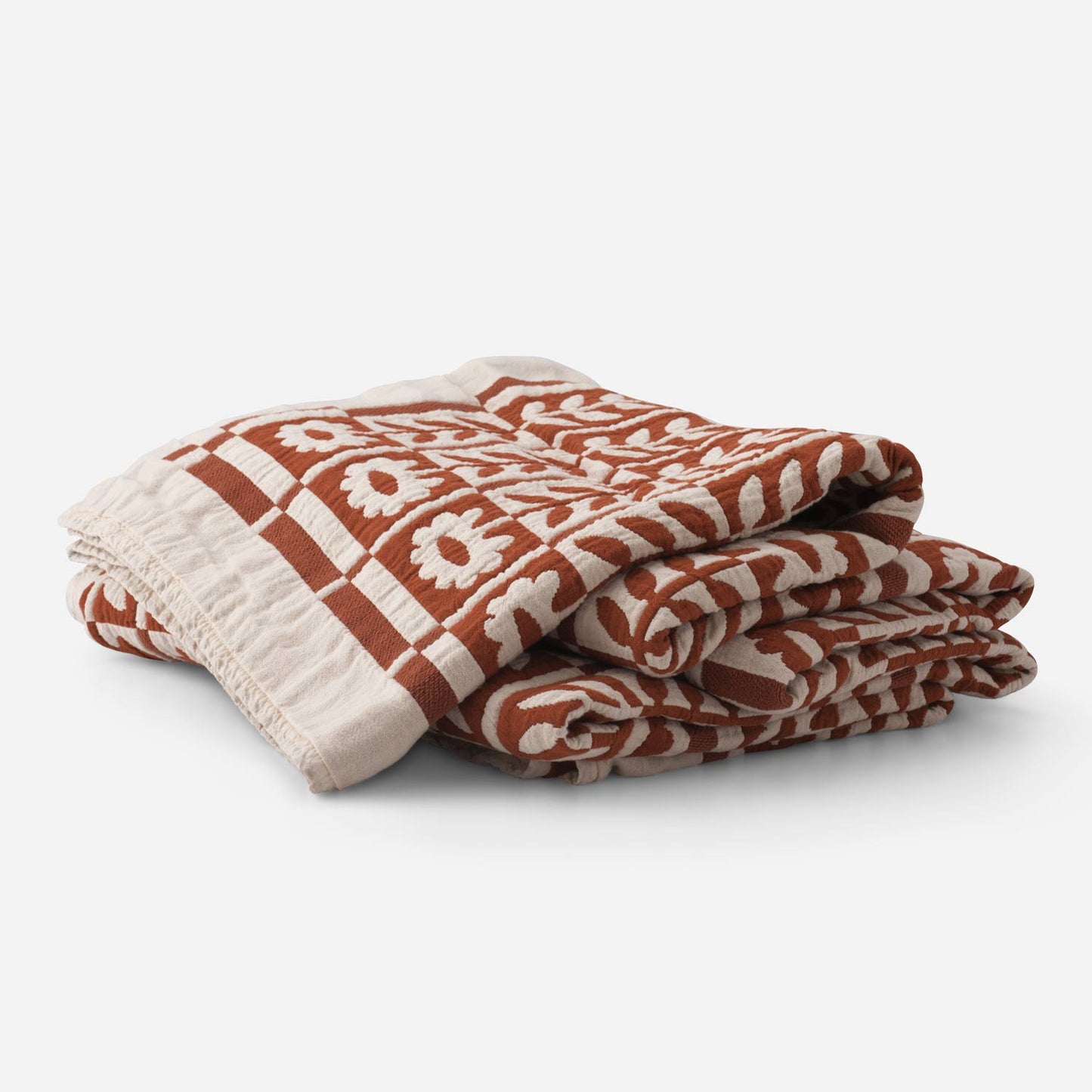 Angled view of folded Stillwater Floral Quilt showing rust and cream mirrored floral jacquard texture, 100% cotton on white