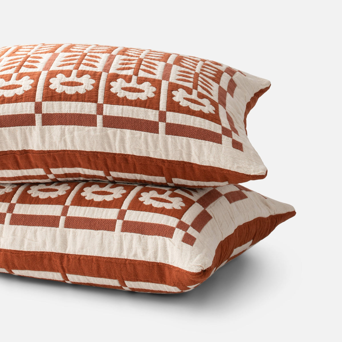 Angled view of Stillwater sham showcasing a rust and cream geometric floral pattern on a white background