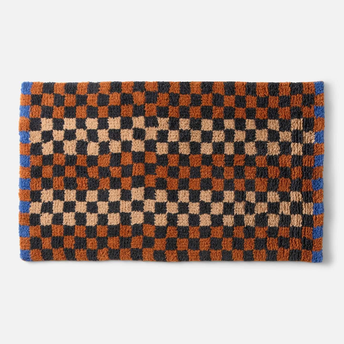 Top edge view of Felix shag rug showing high-pile checkerboard in butterscotch, black and rust with blue border on white background