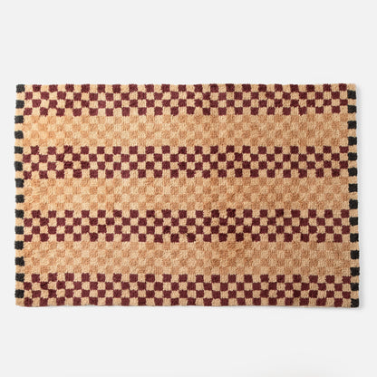 Top edge of Schoolhouse x Clare V. Felix shag wool rug showing butterscotch and burgundy checkered pattern with black border on white background