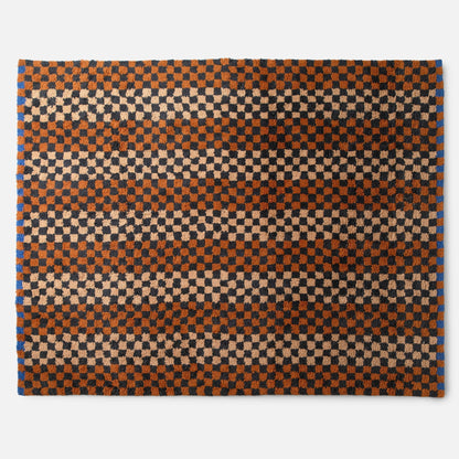 Top-edge view of Felix shag wool rug showcasing high-pile checkerboard in butterscotch, charcoal and cream on white