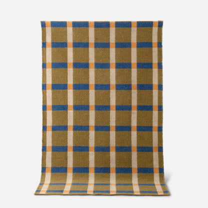 Top-down view of Plaid Wool Reversible Rug showing blue and orange plaid on olive and cream wool on white background