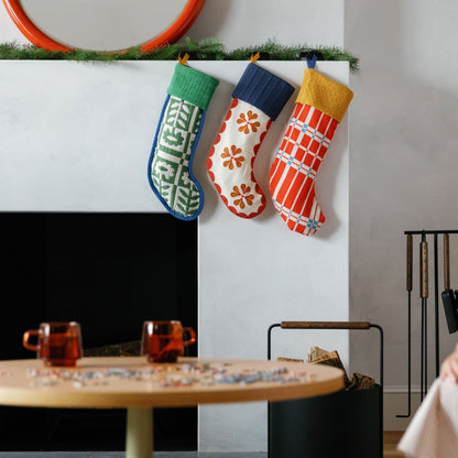 Three colorful patterned stockings hang from a wall ledge in a cozy living room