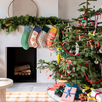 Holiday mantel displays colorful stockings beside a decorated Christmas tree