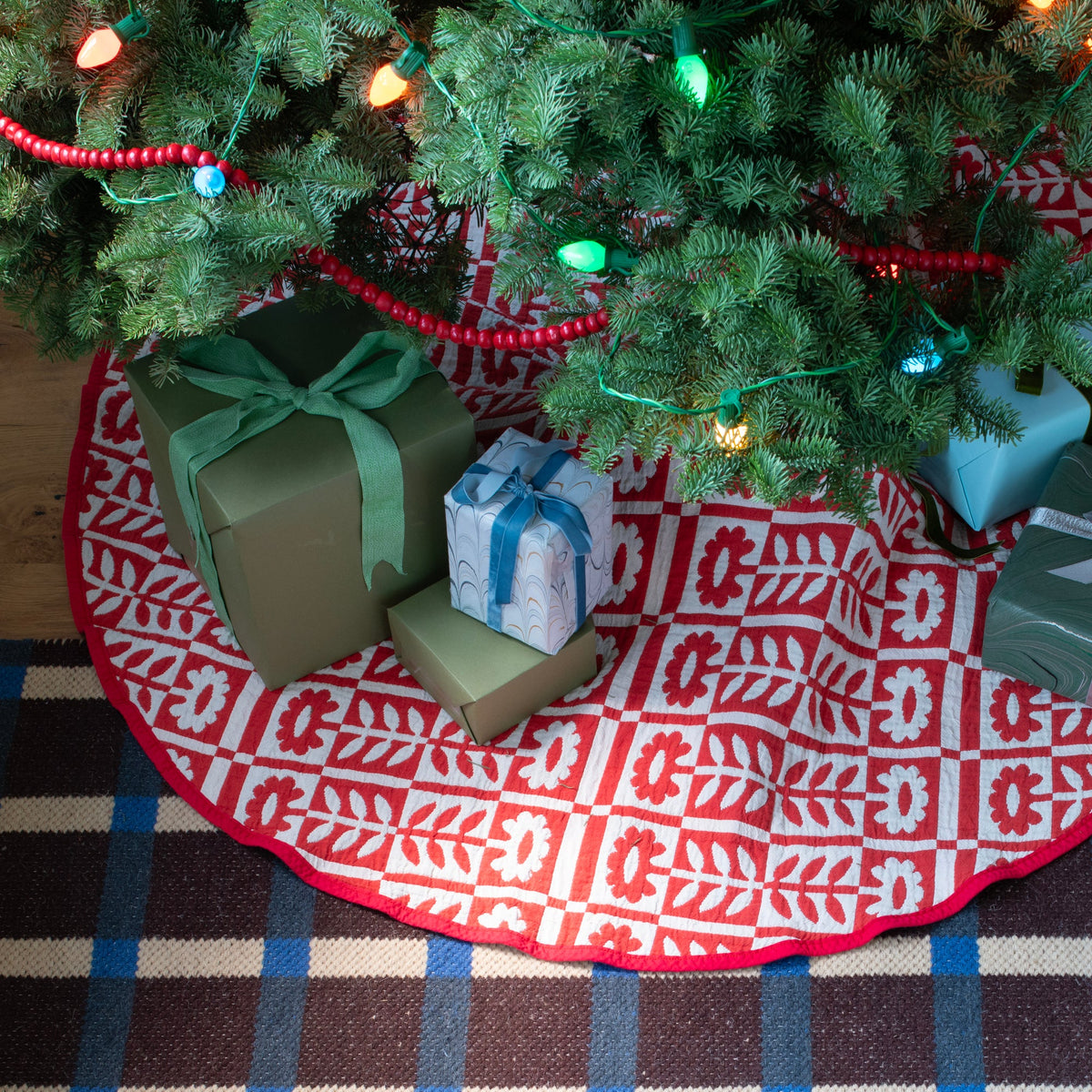 Angled view of Stillwater Tree Skirt showing its red and white floral pattern beneath a Christmas tree with gifts