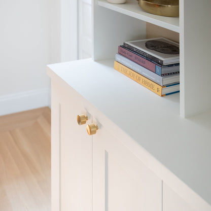 Angled view of Mid Century Knob showcasing round gold-tone knobs with a white cabinet and bookshelves in background