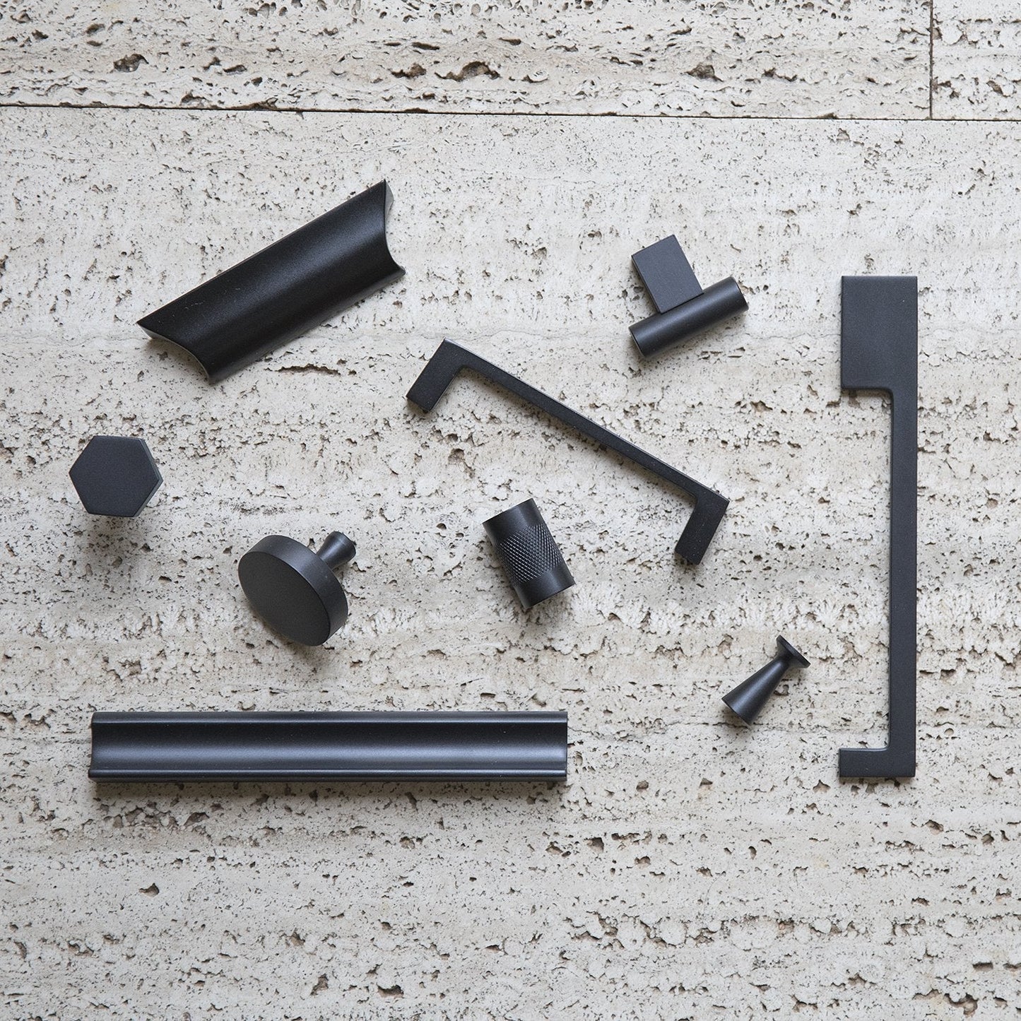 Top view of True Black T Pull with cylindrical bar and rectangular mount among assorted hardware on textured stone
