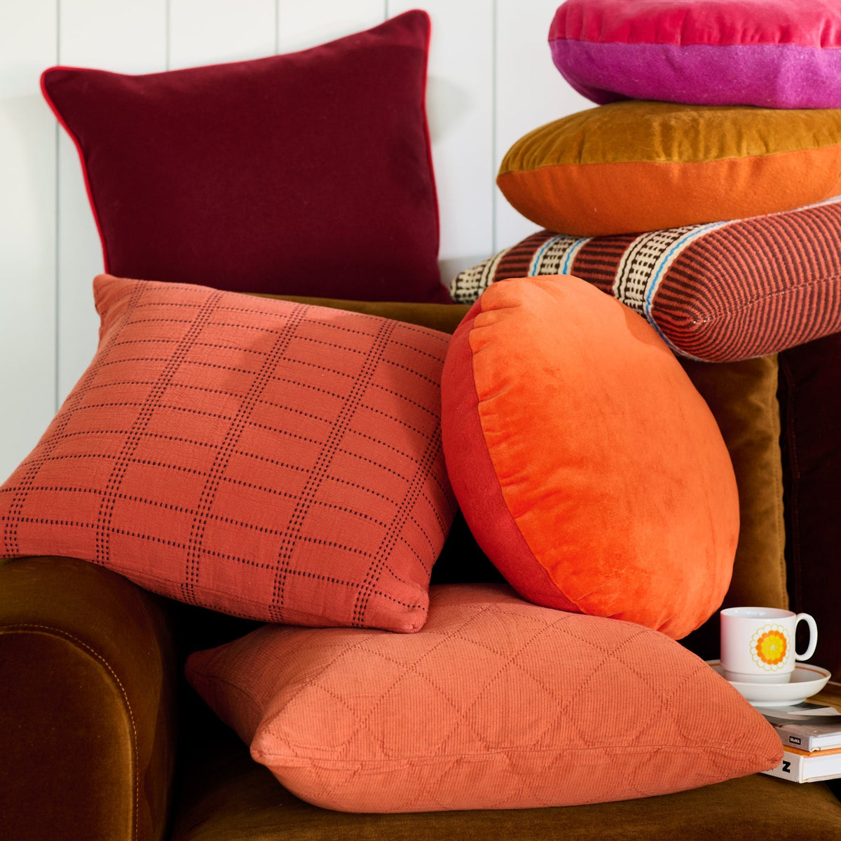 Colorful pillows arranged on a brown chair beside books and a teacup
