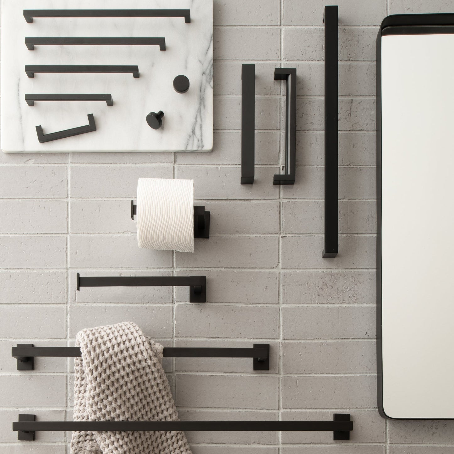 Black Edgecliff pulls and bathroom hardware displayed on a gray brick wall beside a mirror