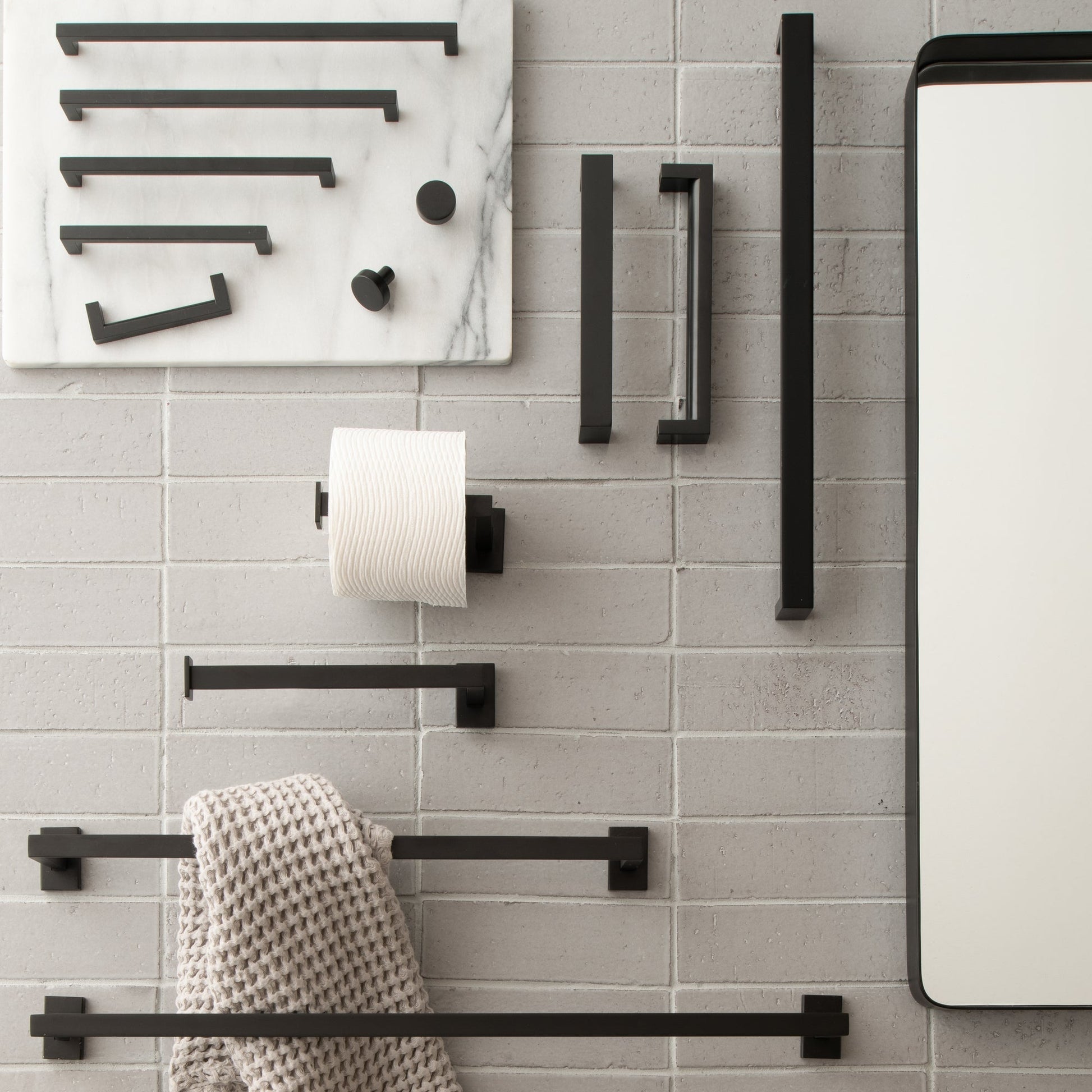 Black Edgecliff pulls and bathroom hardware displayed on a gray brick wall beside a mirror
