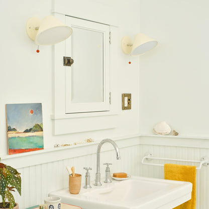Two Ecru-Gloss Clare V Hans wall sconces flank a medicine cabinet in a bright bathroom