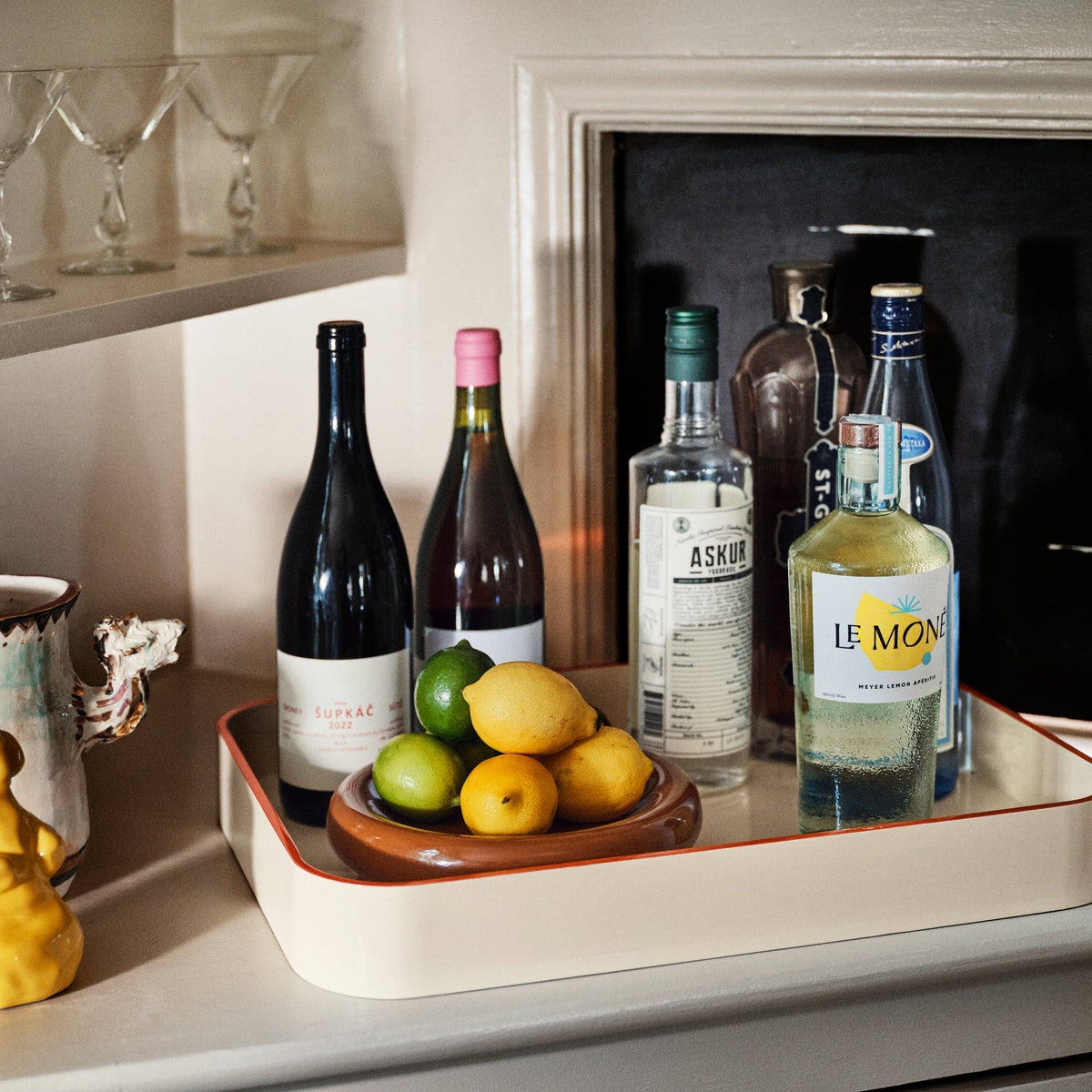 Angled view of Clare V Sonia Tray showcasing raised cream sides and red trim with bottles and citrus on a counter