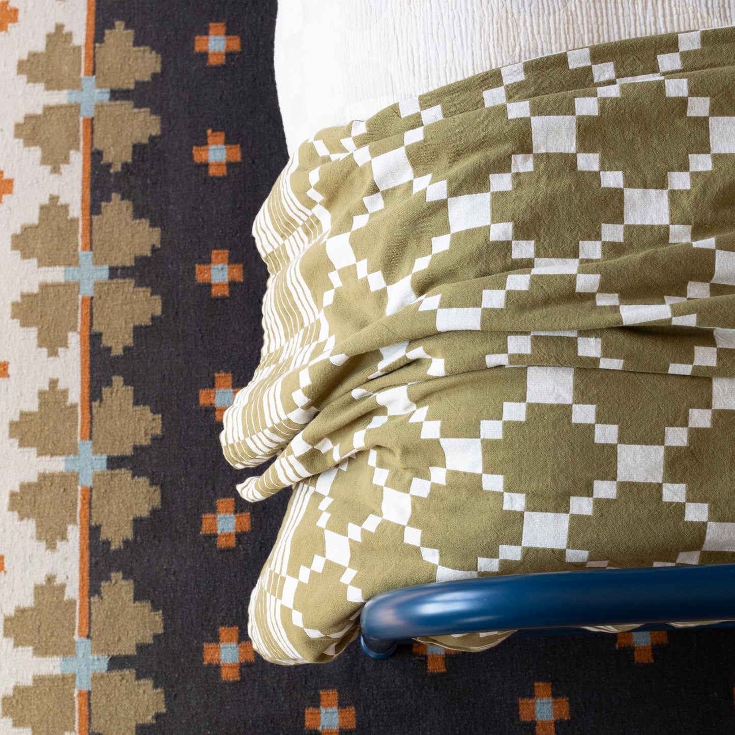 Overhead view of Flora Wool Flatweave Rug showing geometric folk-floral pattern and flatwoven texture with bed and chair