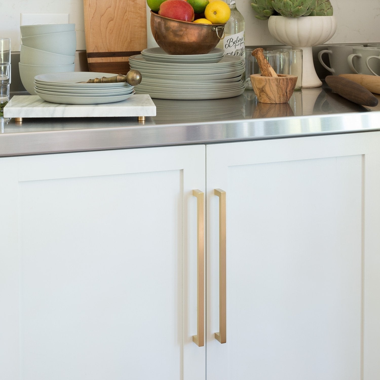 Installed view of Edgecliff Appliance Pull showcasing vertical bar design on white kitchen cabinets with a styled countertop