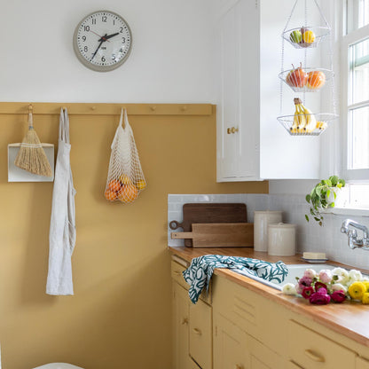 Bright kitchen with mustard cabinets, wood countertop, sink, wall hooks, hanging produce baskets, and flowers