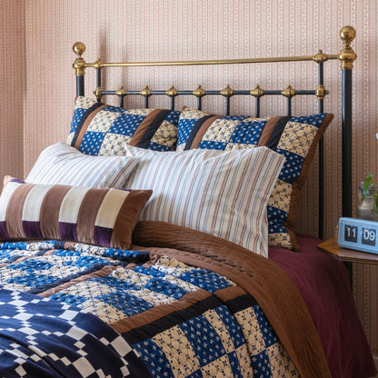 Close-up view of Albright Quilt showcasing blue, cream, and brown patchwork on a bed in a patterned bedroom