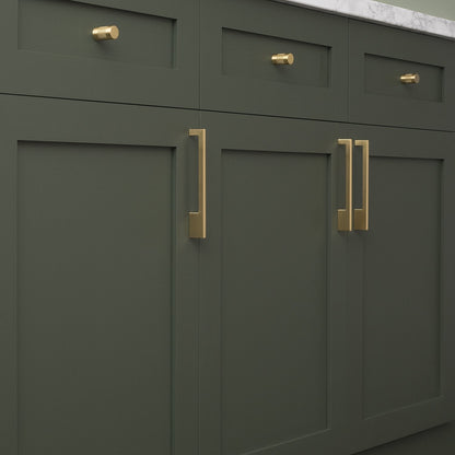 Natural brass knurled knobs adorn dark green kitchen cabinets beneath a marble countertop