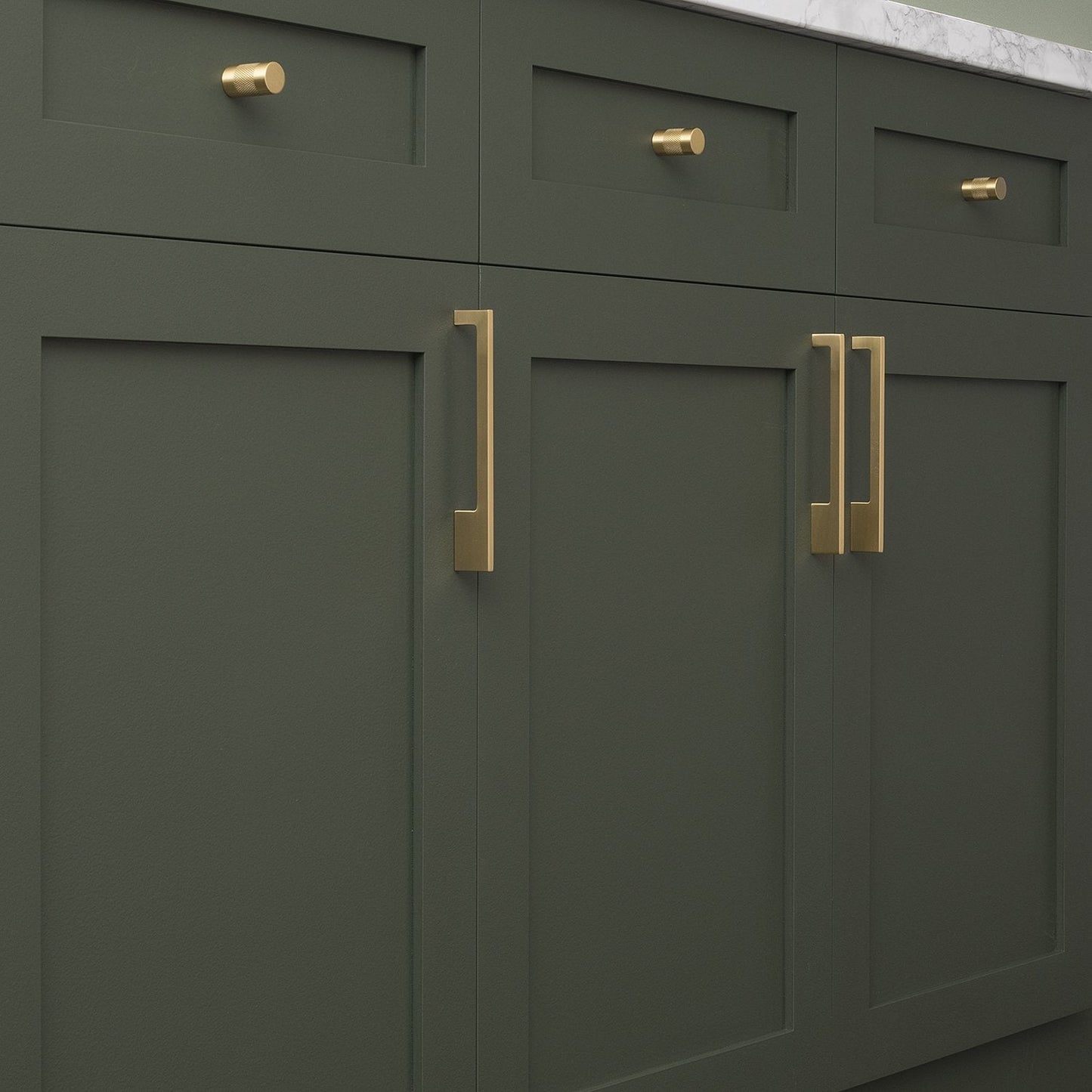 Close-up of Alberta Pull showcasing its asymmetrical brass design on dark green cabinetry