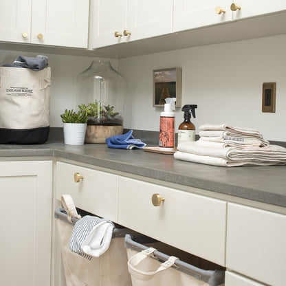 Natural brass Riverwood knobs installed on white cabinets in a laundry room