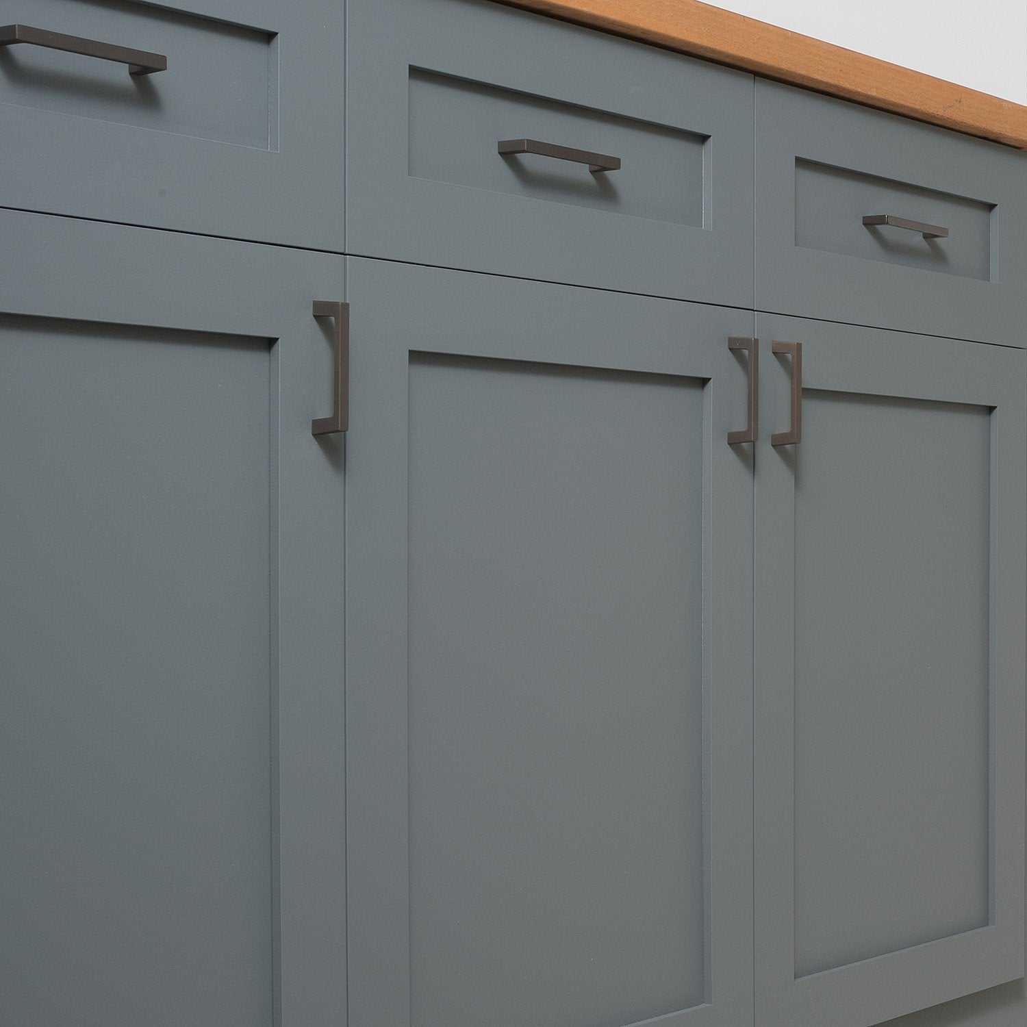 Close-up of Greenwood Pull showcasing its thin profile on blue-gray paneled cabinets