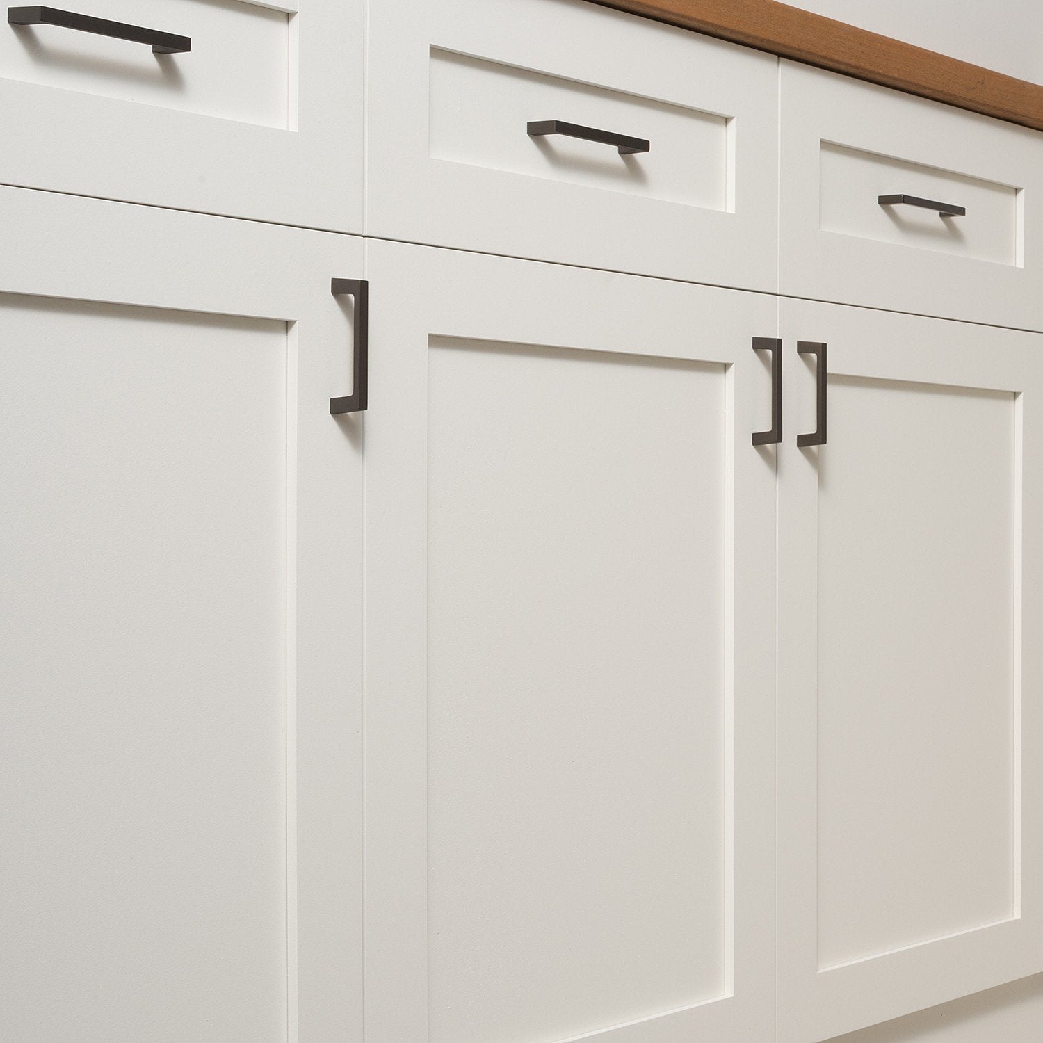Greenwood cabinet pulls installed on white paneled cabinets beneath a wood countertop