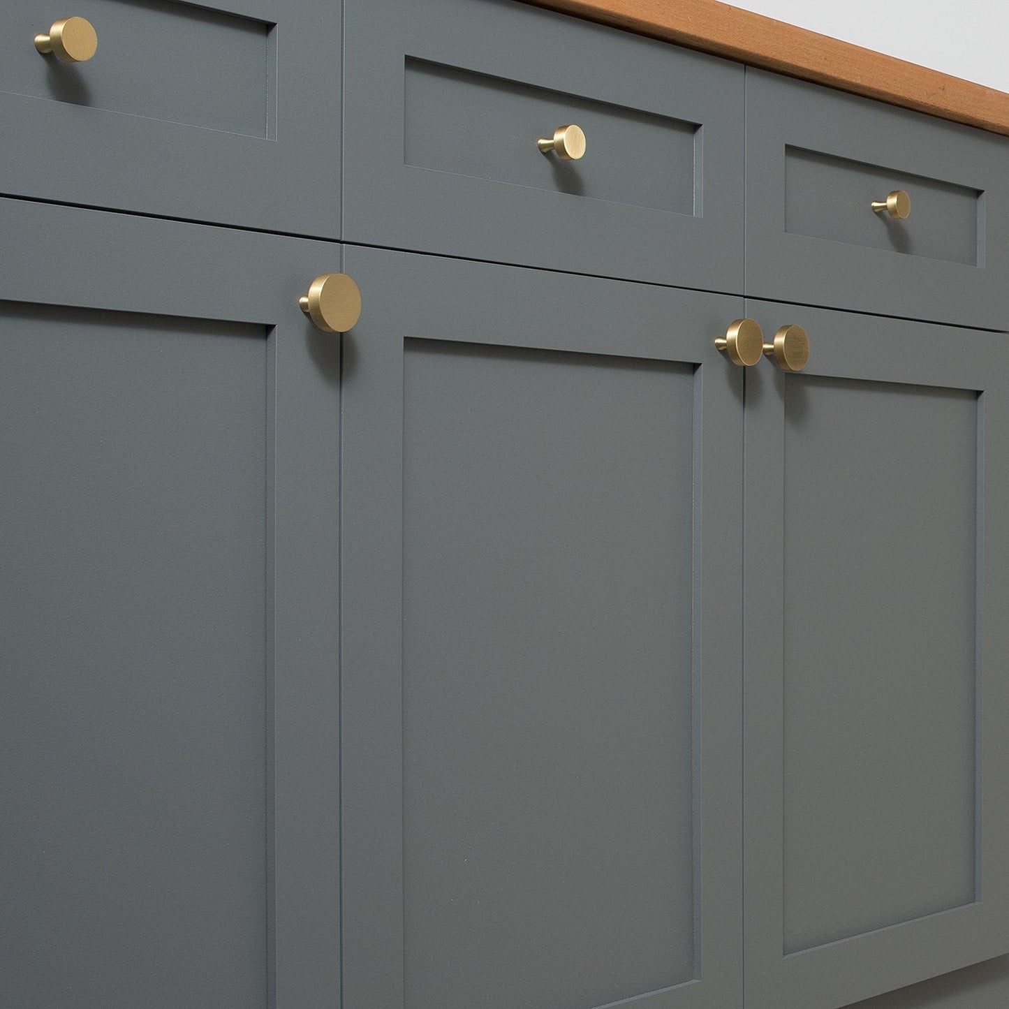 Natural brass Riverwood knobs installed on dark gray paneled cabinet doors with a wood countertop