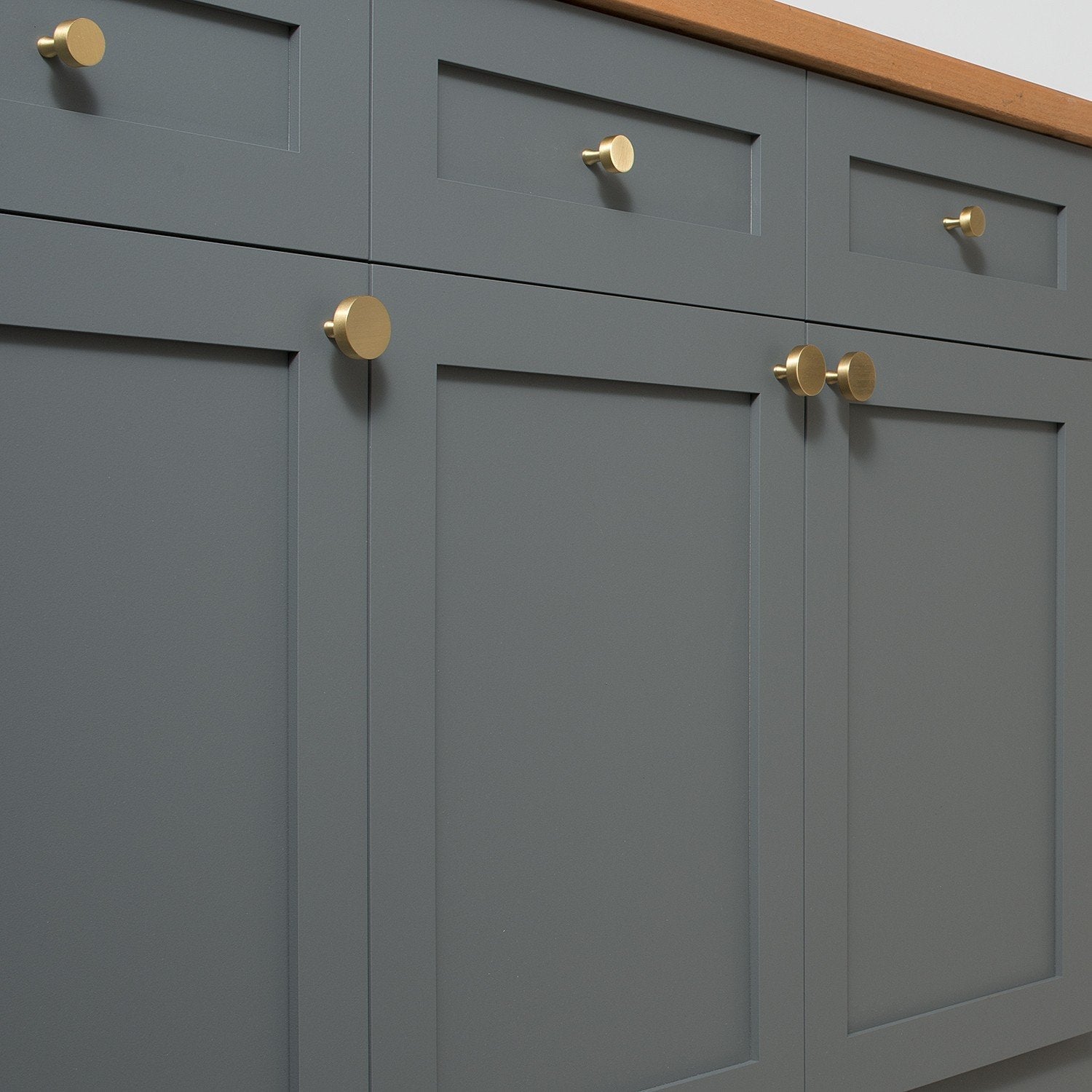 Natural brass Riverwood knobs installed on dark gray paneled cabinet doors with a wood countertop