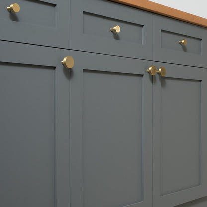Natural brass Riverwood knobs installed on dark gray paneled cabinet doors with a wood countertop