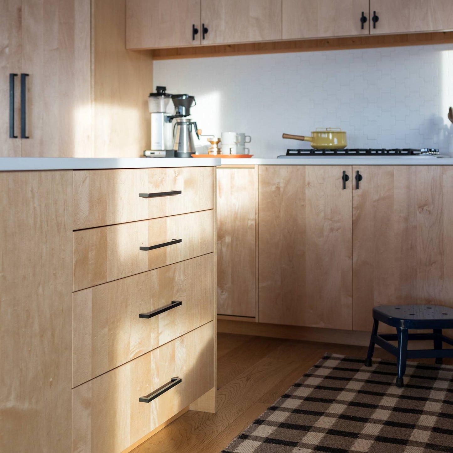 Black Edgecliff appliance pulls on light wood kitchen cabinets with a coffee maker and stove