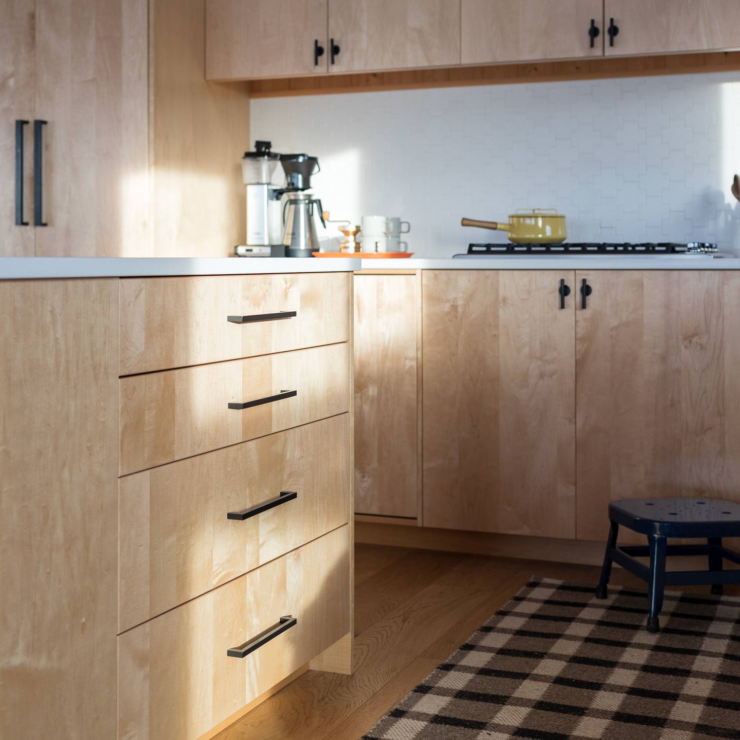 Black Edgecliff appliance pulls on light wood kitchen cabinets with a coffee maker and stove