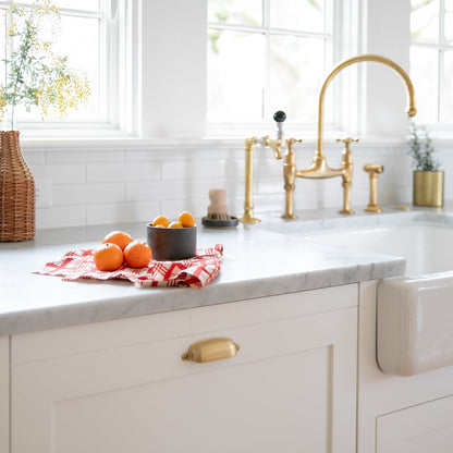 Close view of Brunswick Pull showcasing its solid brass finish and exposed mounting hardware on a white kitchen cabinet
