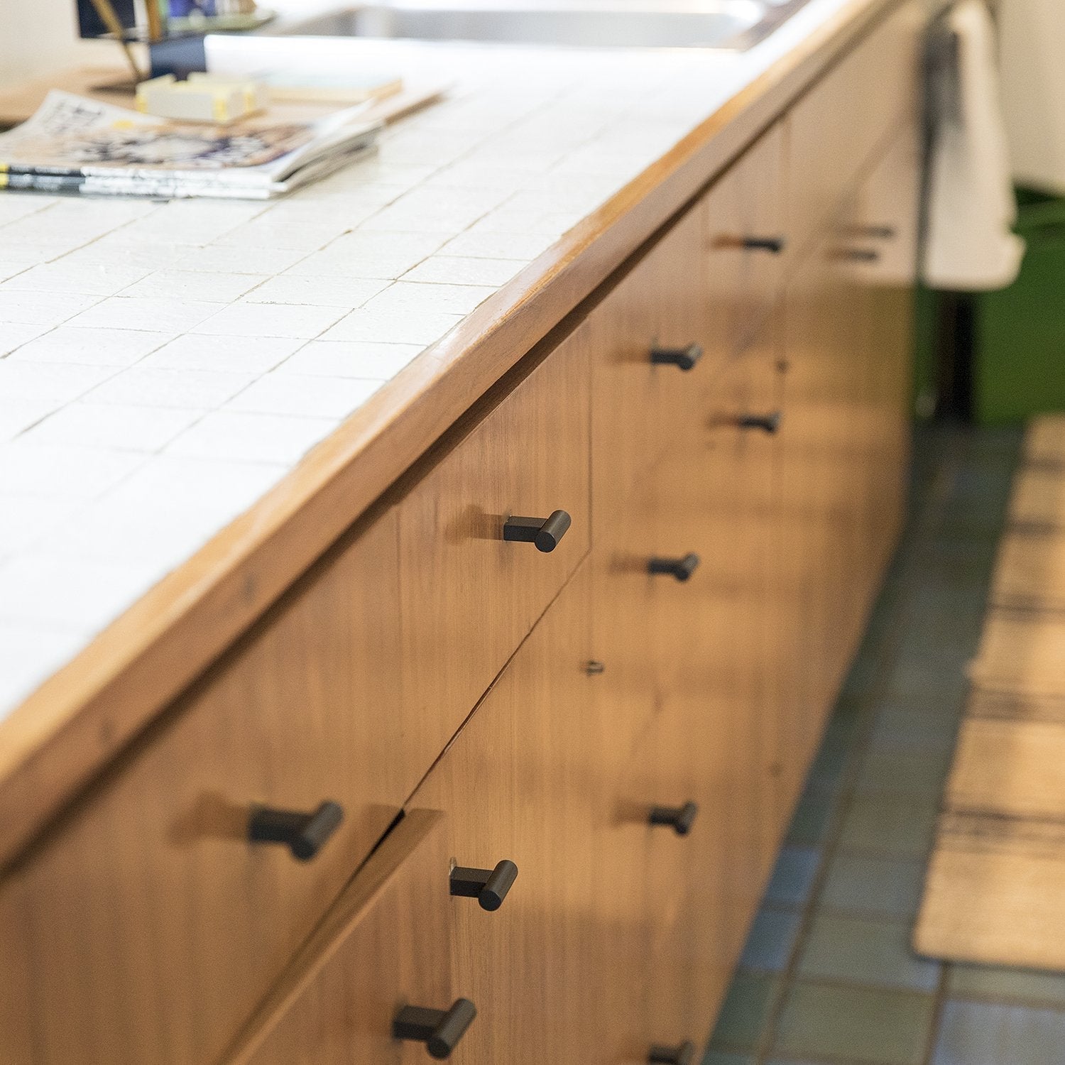Black T Pulls installed on warm wood cabinetry beside a tiled countertop