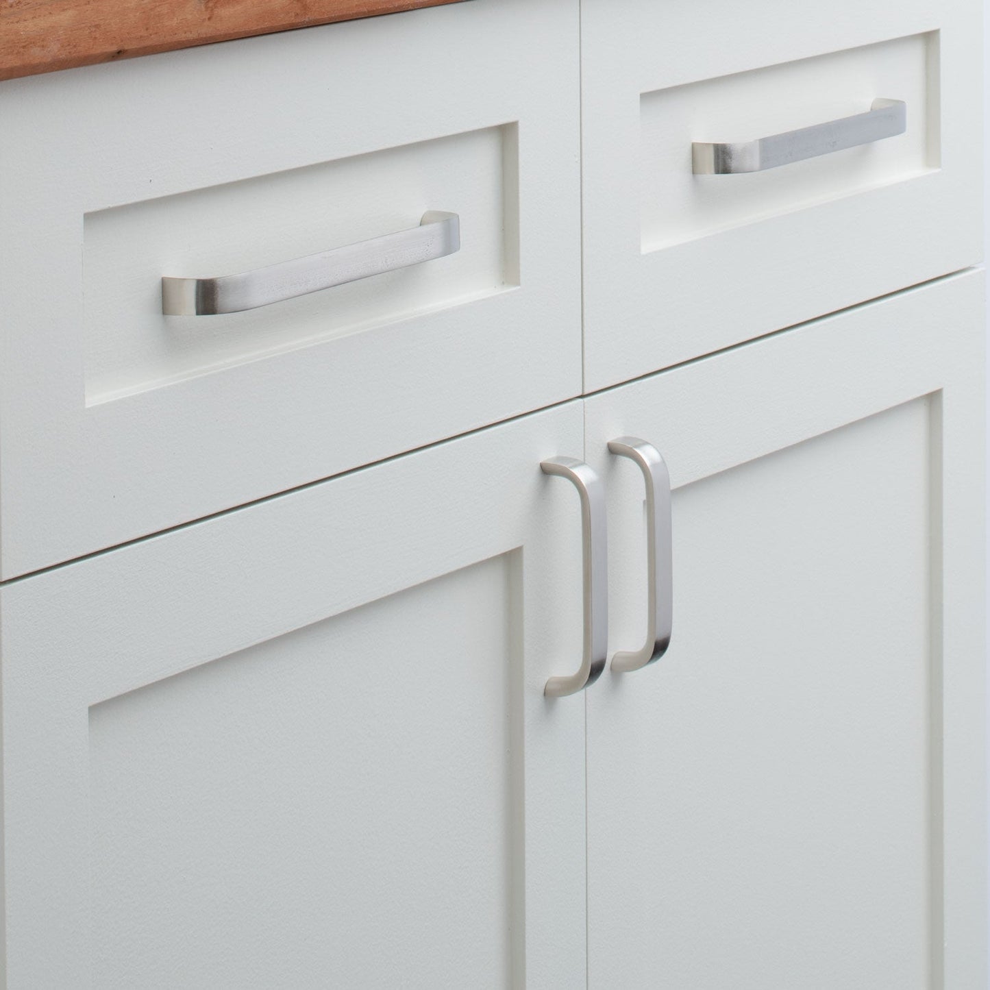 Close-up of Cascade Pull showcasing curved silver handles on white paneled cabinets