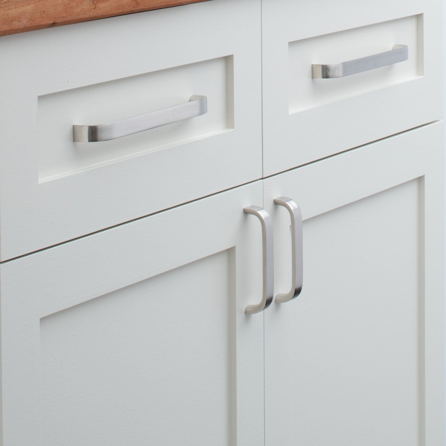 Close-up of Cascade Pull showcasing curved silver handles on white paneled cabinets